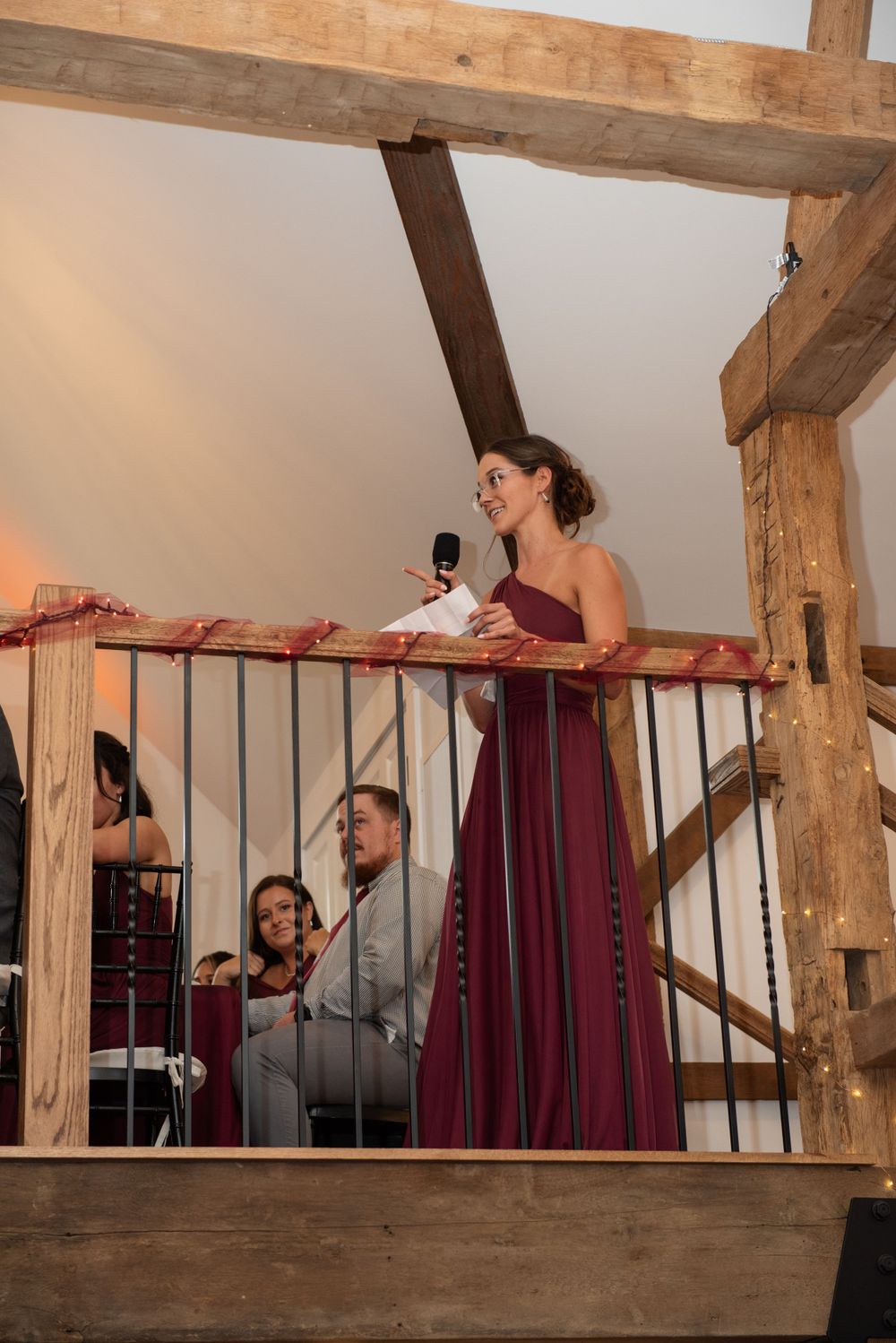 Speaker in burgundy dress delivering speech from rustic wooden balcony.