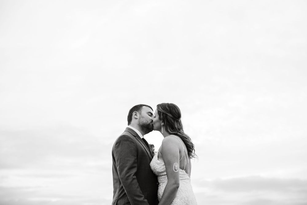 A romantic black and white portrait of a couple embracing against an overcast sky.
