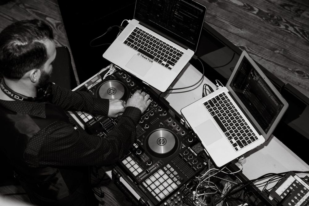 DJ equipment setup with laptops and controllers on wooden surface in dark lighting.