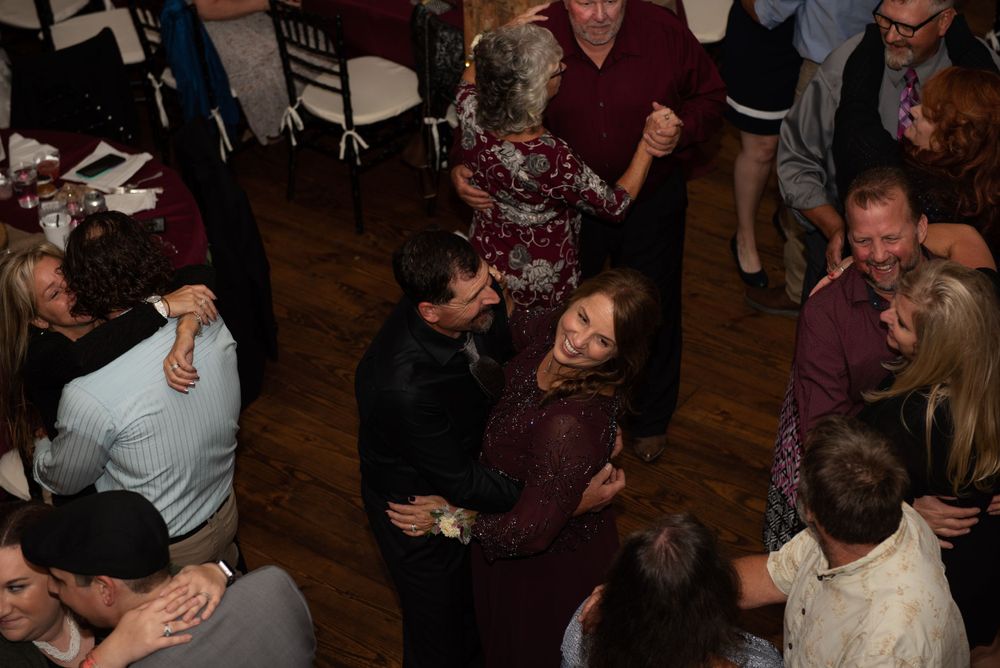 Wedding guests dancing and celebrating on a wooden dance floor at an indoor reception.