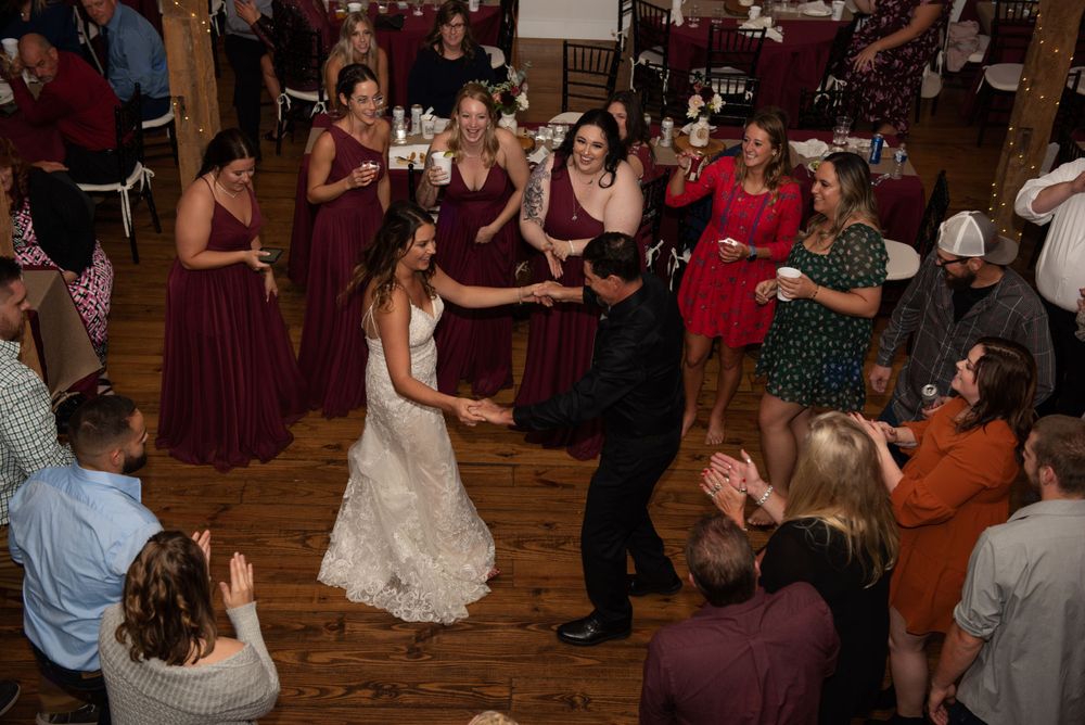 Wedding party and guests dancing in burgundy dresses on wooden dance floor at indoor reception.