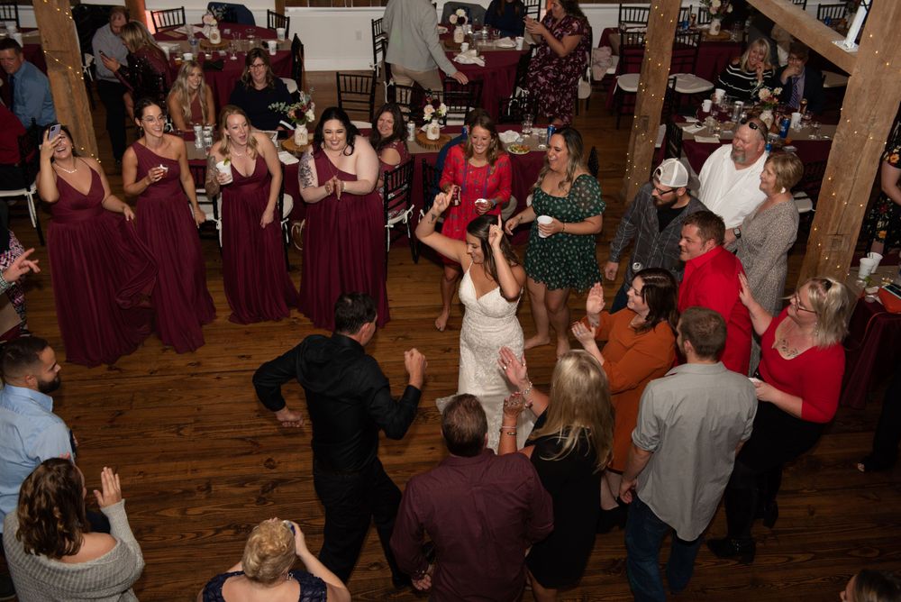 Lively wedding reception with dancers in burgundy bridesmaid dresses on hardwood floors.