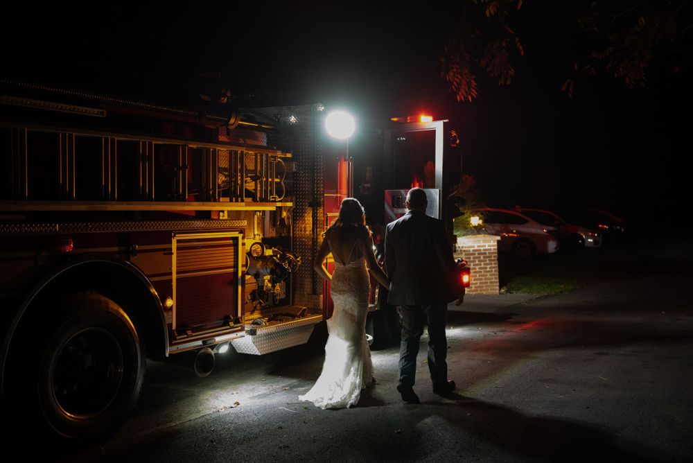 Silhouetted couple stands near a fire truck at night with dramatic lighting.