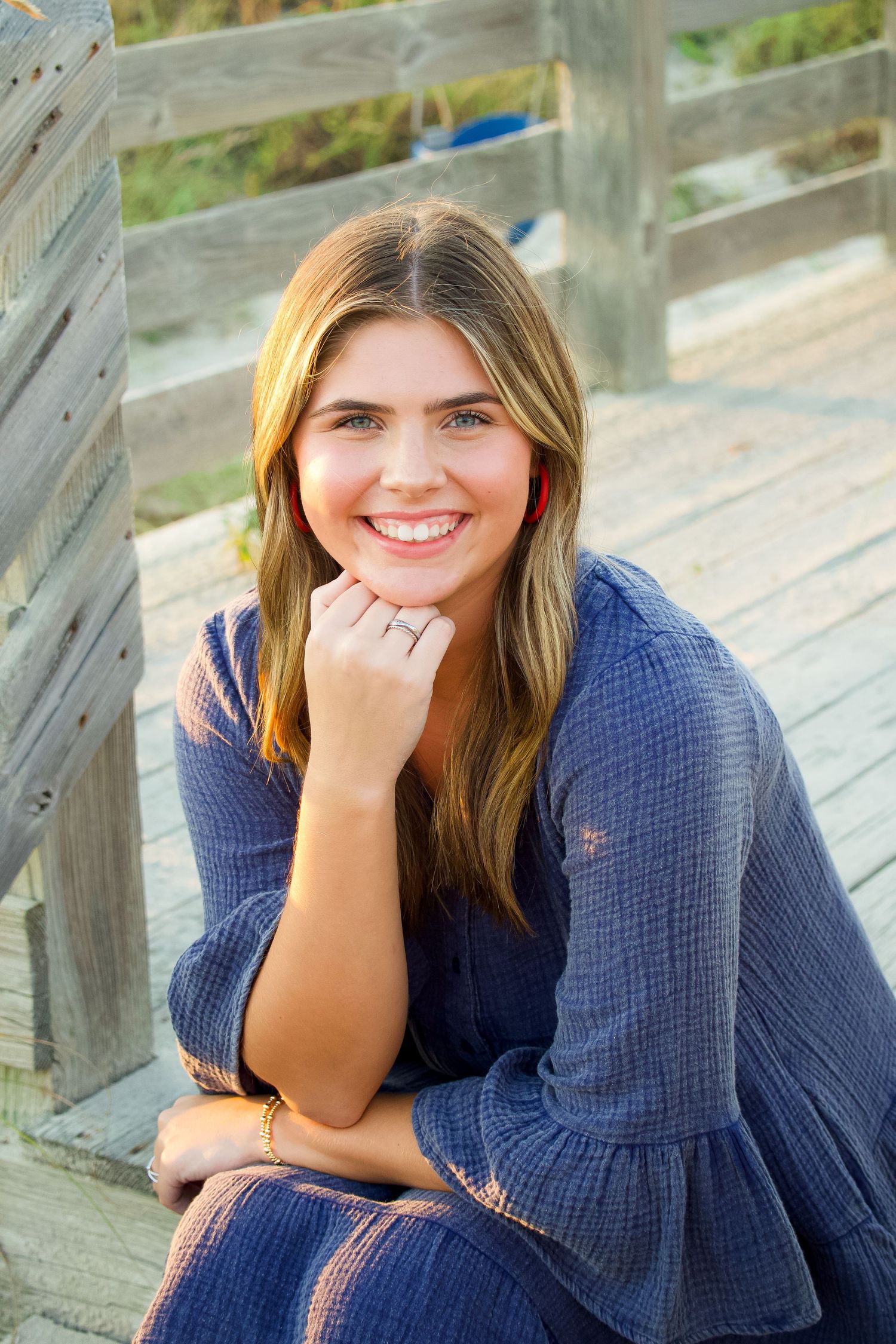 Casual portrait of someone in a blue sweater sitting on wooden steps outdoors.