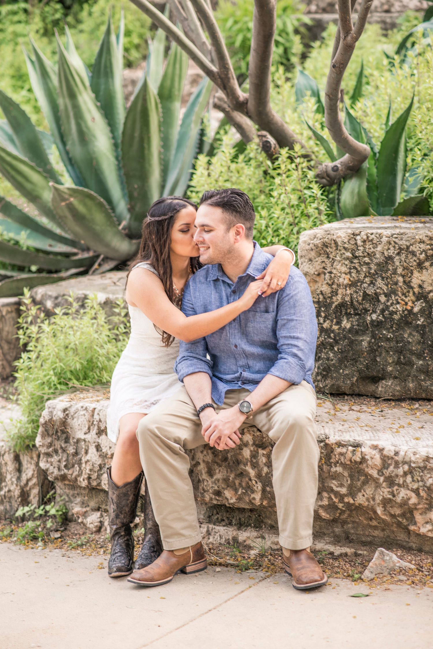 A couple sits on stone steps surrounded by agave plants and desert landscaping.