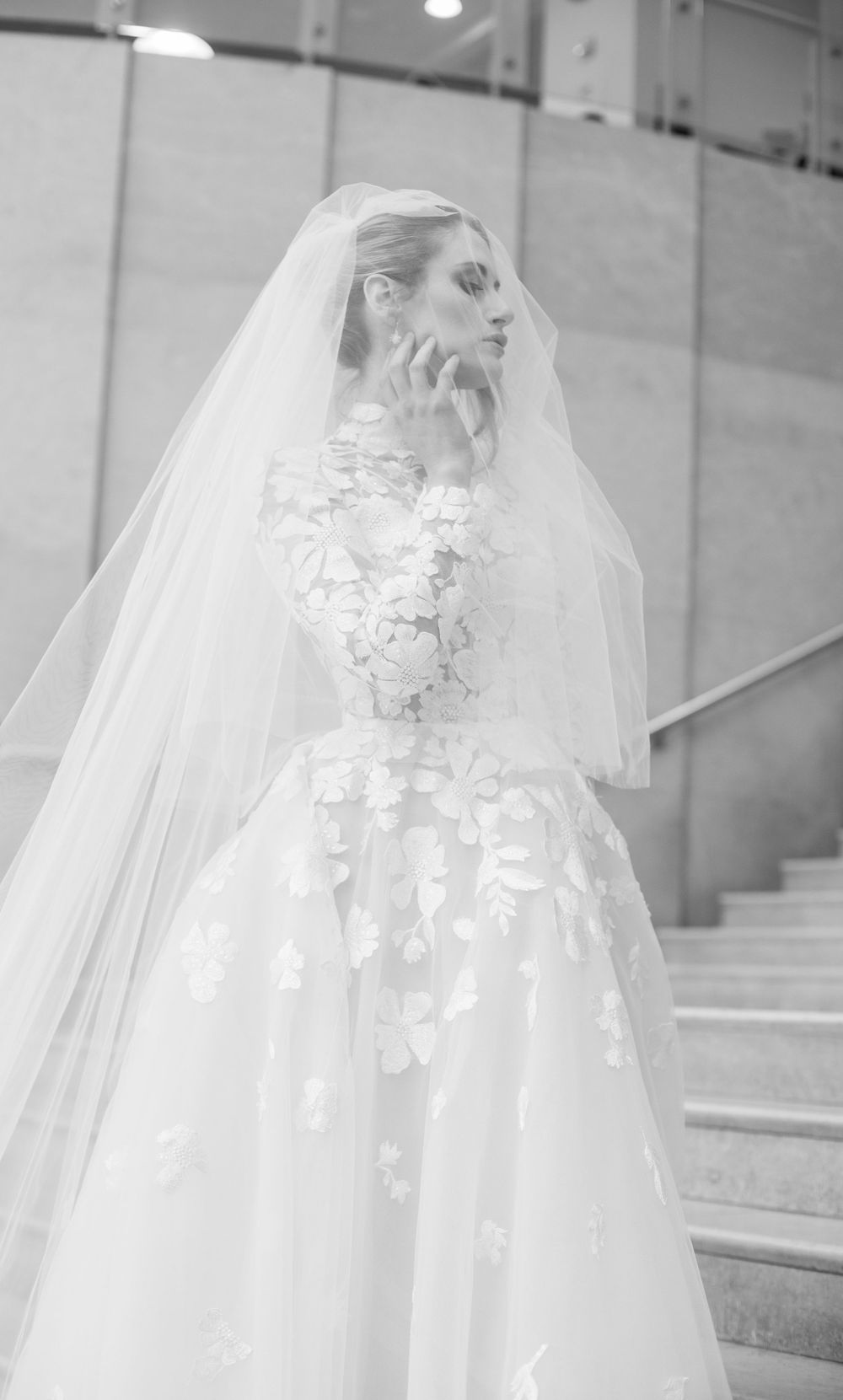 A stunning lace wedding gown with floral appliques and flowing cathedral veil photographed in black and white.