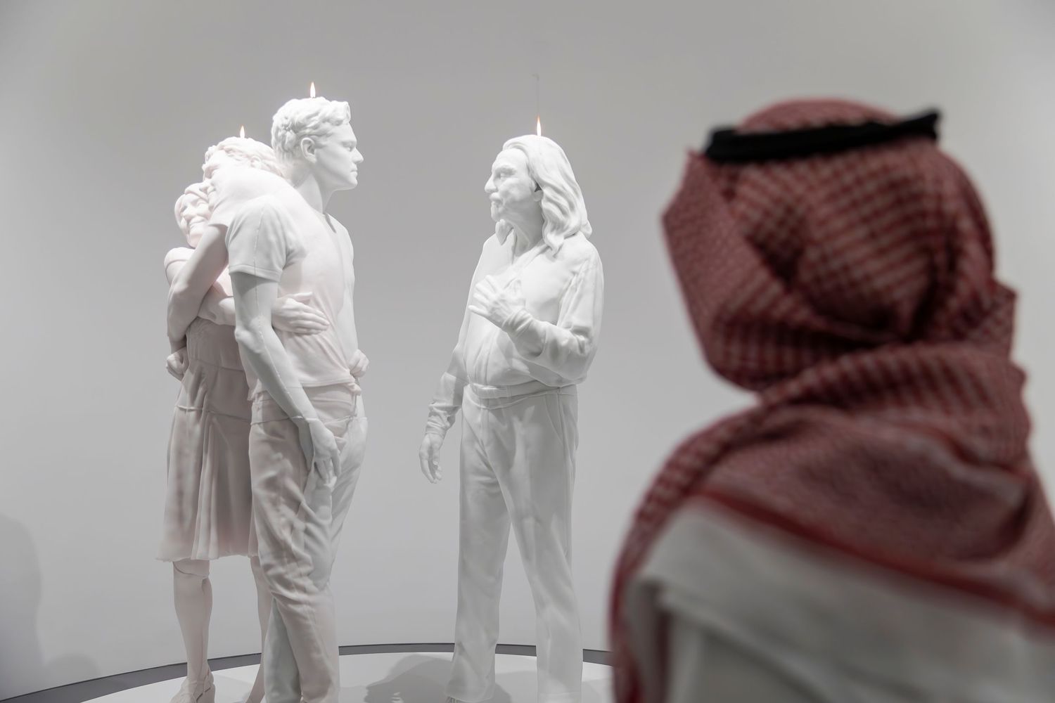 Museum visitor observes white sculptural figures in traditional Middle Eastern dress.