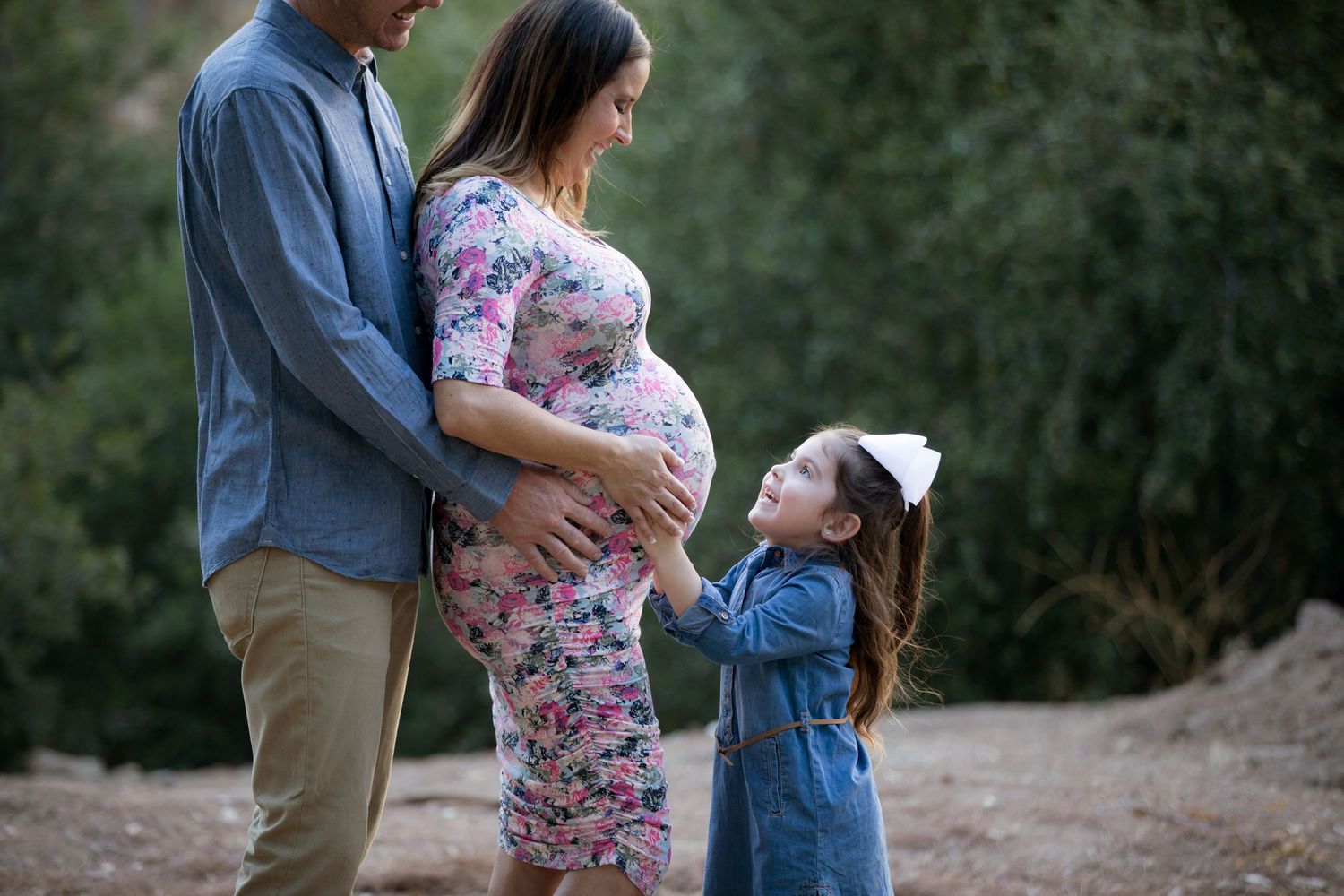 A tender family moment outdoors with an expectant mother in a floral dress.