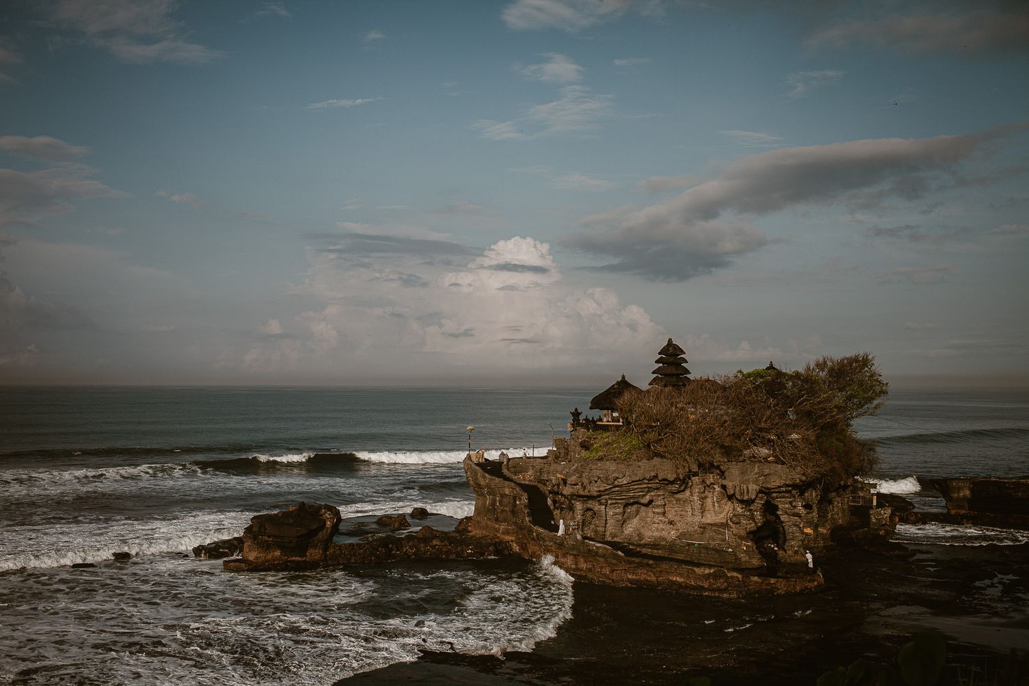 Tanah Lot Temple Bali at high tide with morning sun and cloudy sky
