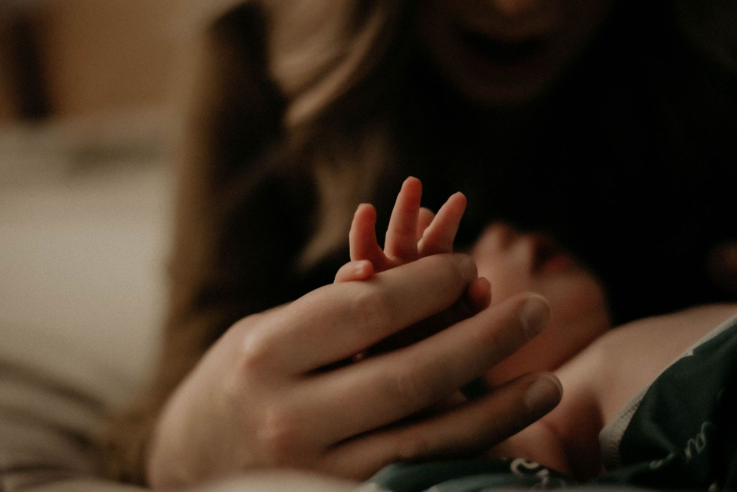 Gentle hands cradle tiny newborn fingers in an intimate indoor setting.