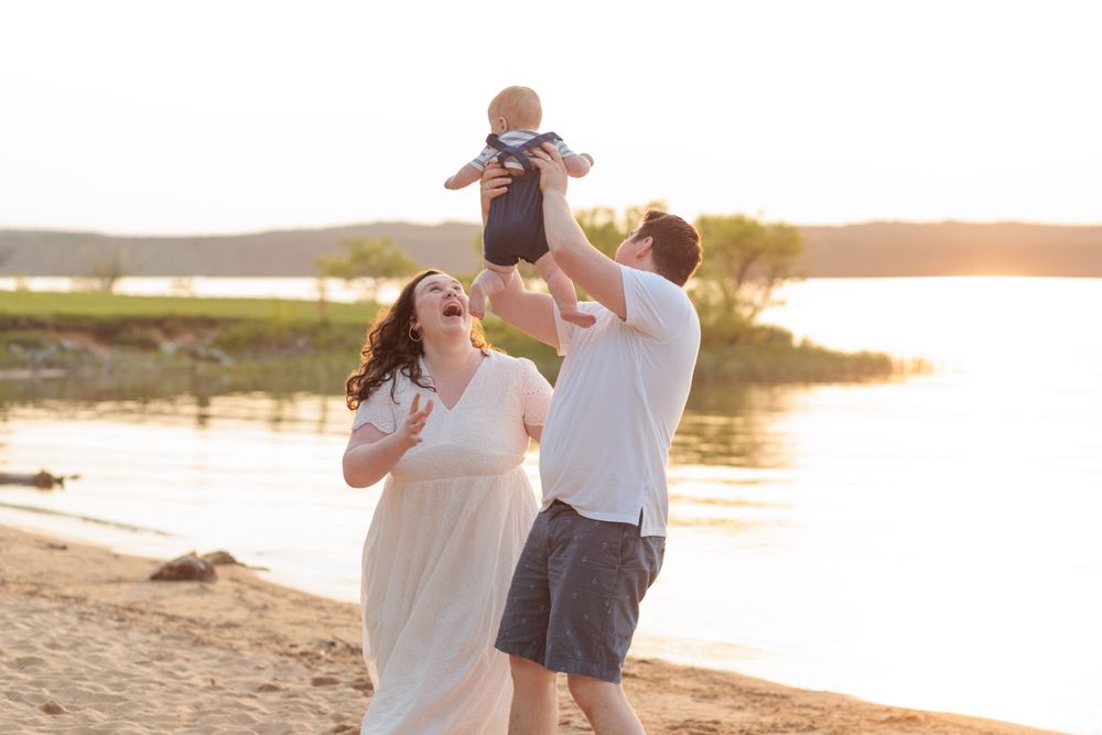 A family plays together on a beach at sunset, lifting a child in the air while laughing and enjoying the golden light.