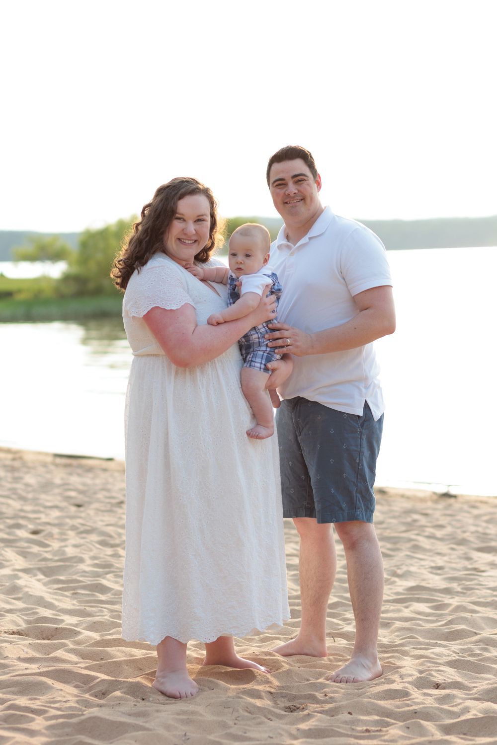 A family stands together on a sandy beach near the water on a sunny afternoon.