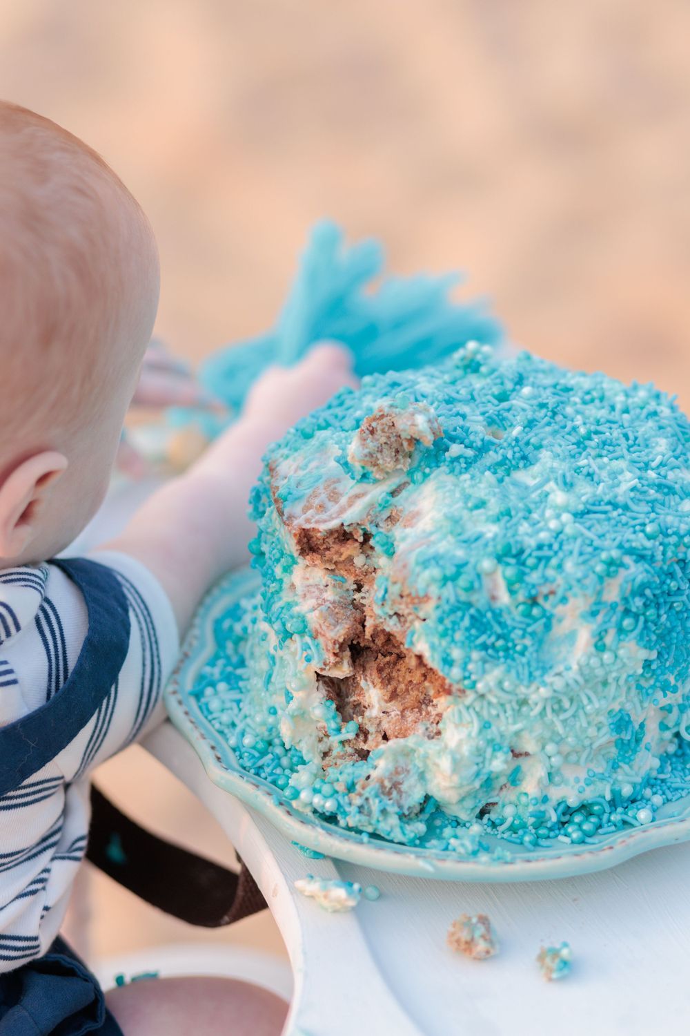 Baby reaches for bright blue smash cake with crumbs and frosting during first birthday photo session in Raleigh.