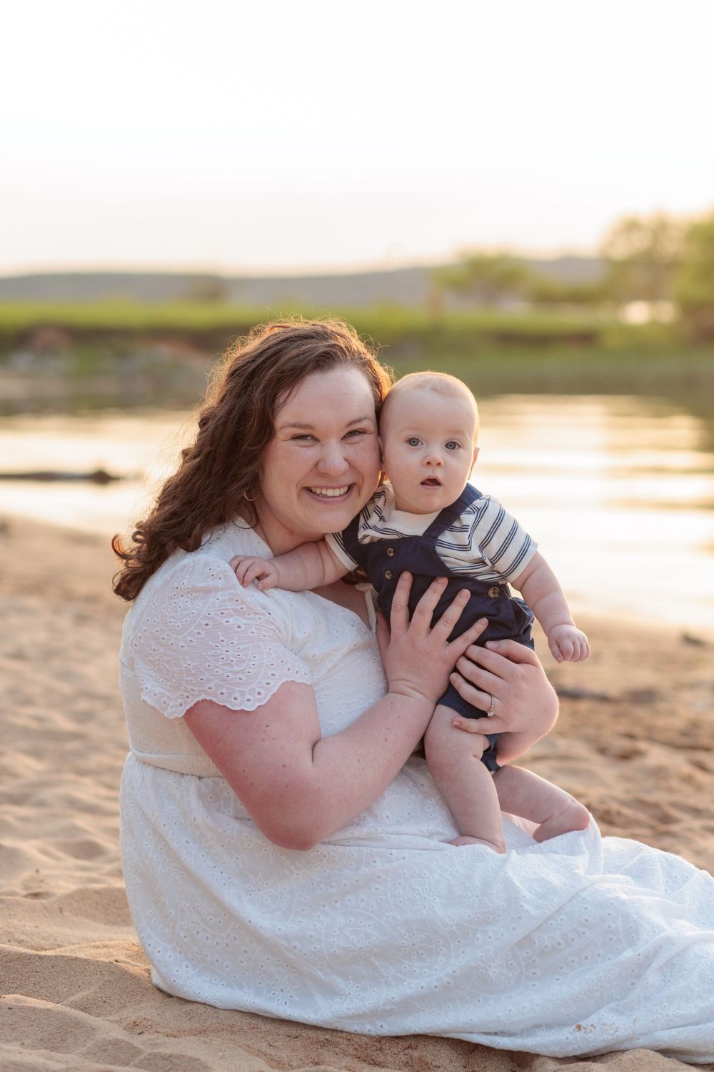 A heartwarming beach portrait at sunset showing a tender moment between parent and infant on golden sand.