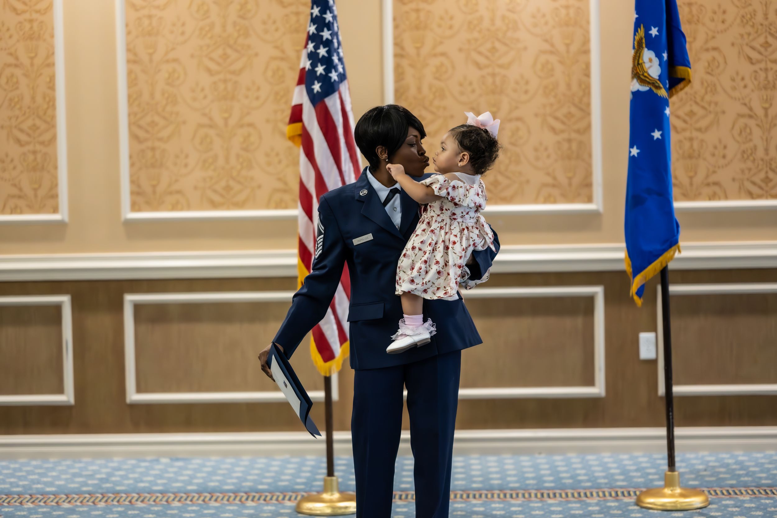 Service members and family celebrate in formal attire against a gold-patterned wall with flags.