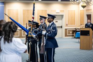 Service members perform ceremonial duties in a carpeted conference room setting.
