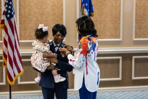 Military ceremony with Air Force member holding small child while others gather near flags.