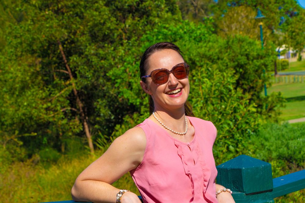 Cheerful figure in pink sleeveless top and sunglasses enjoying sunny day at park.