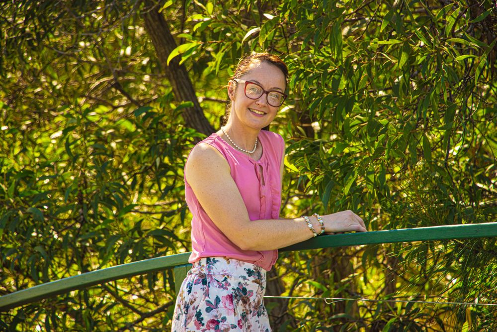 Person in pink top and floral skirt leans on green railing in sunny park setting.