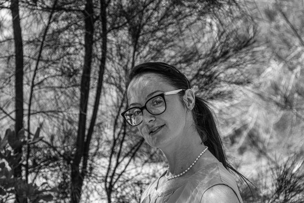 Black and white portrait with glasses in natural outdoor setting.