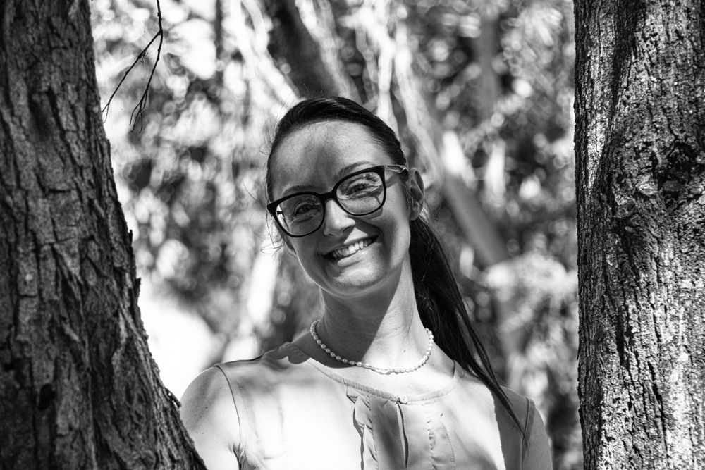 Black and white portrait between trees showing joyful expression and glasses.