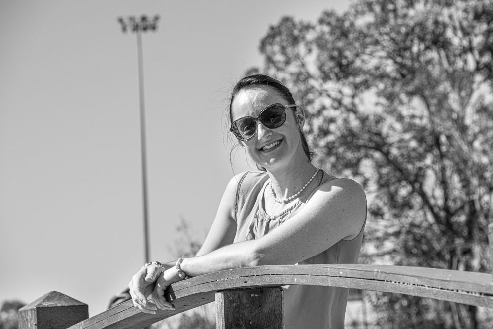 A black and white portrait of someone smiling while holding onto a railing outdoors.