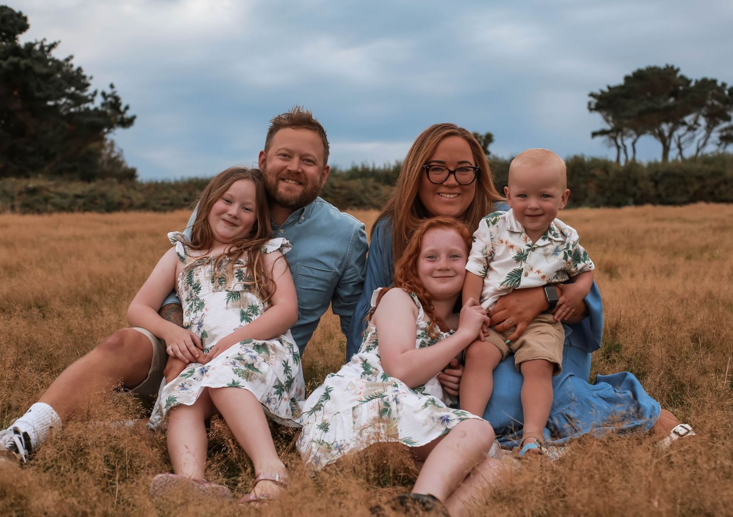 Family group sitting together in grass field on cloudy day.