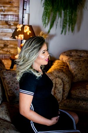 Pregnancy portrait in cozy setting with string lights and hanging plants in background.
