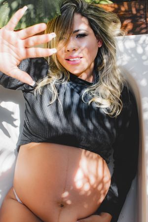 Woman in black crop top poses outdoors with dappled sunlight creating shadows.