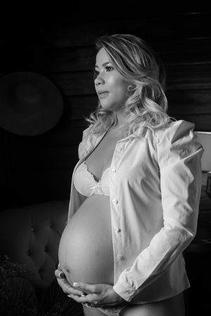 Dramatic black and white portrait in white blouse showing maternity silhouette.