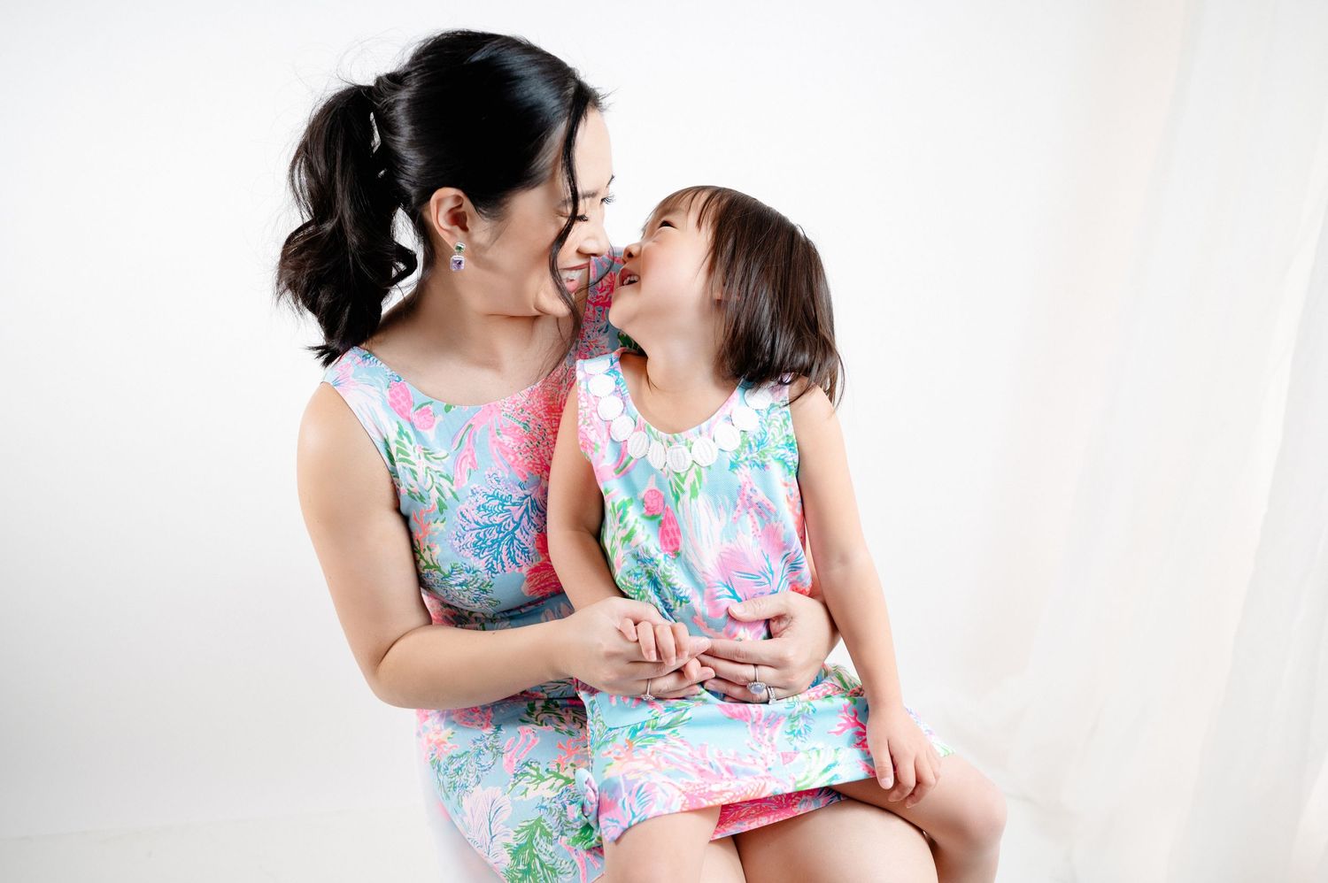 Parent and child wearing matching floral dresses share an intimate moment against a white backdrop.