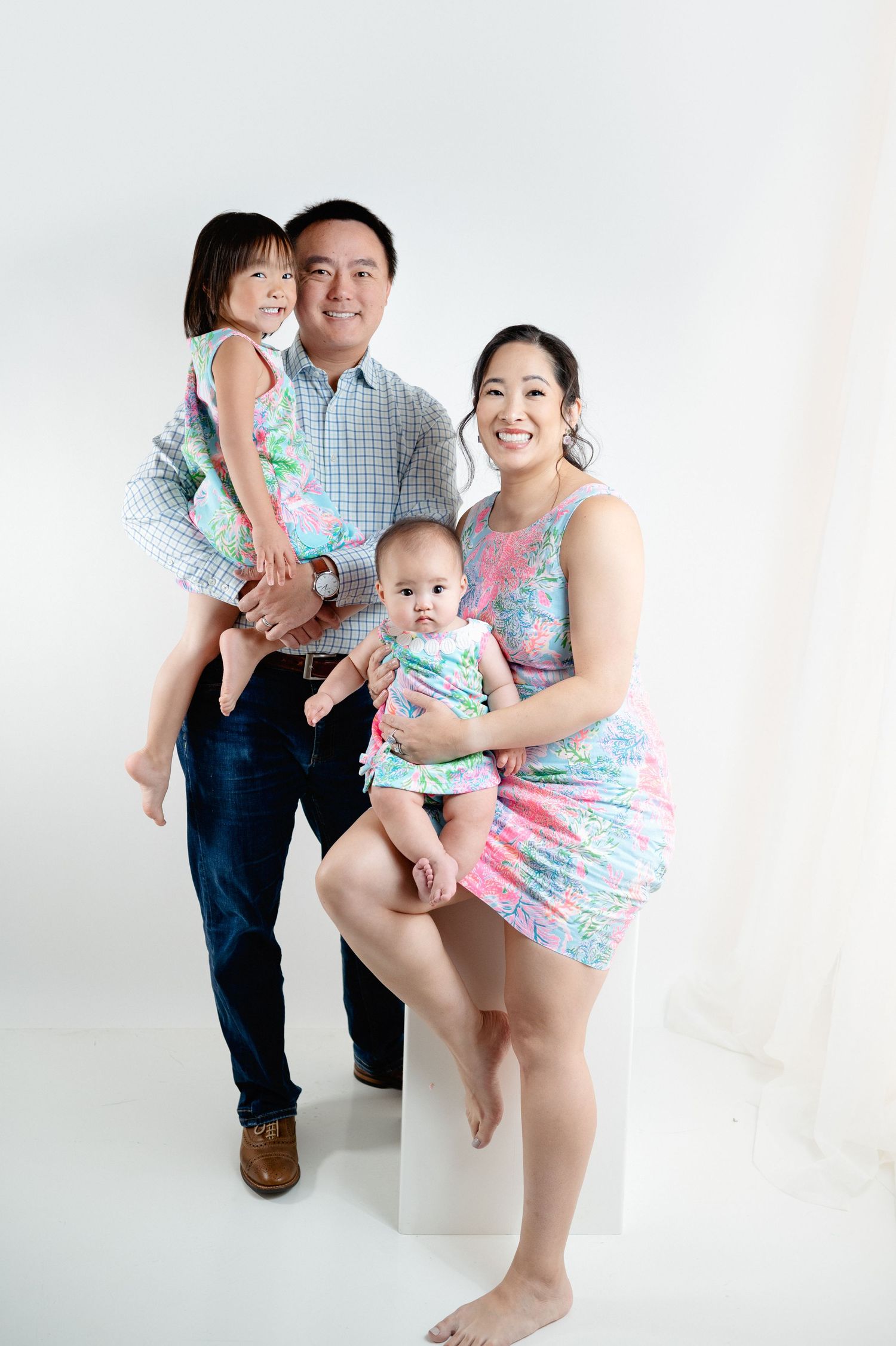 Family of four wearing coordinated blue and pink outfits pose together against white backdrop.