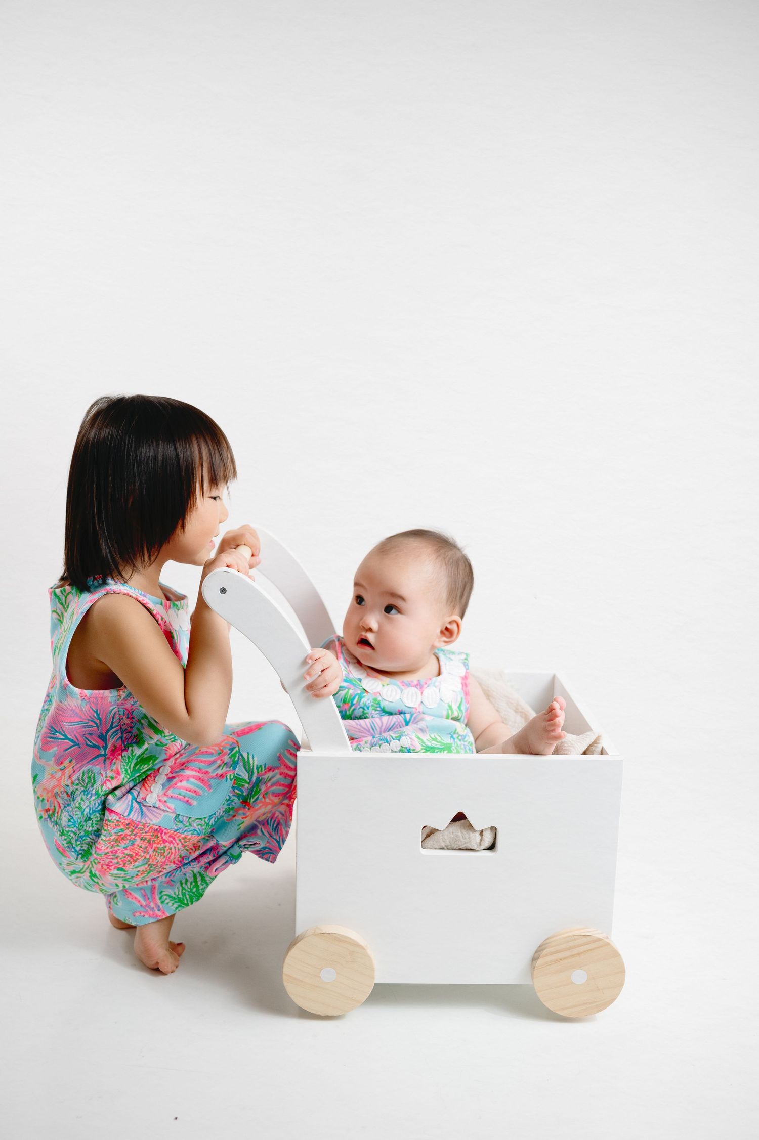 Children playing with white wooden pull cart against minimalist white backdrop.