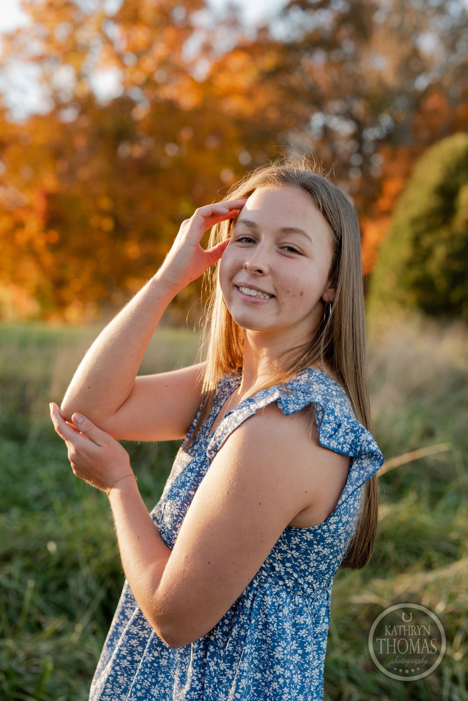A floral blue dress is worn by someone posing in a golden autumn field at sunset.