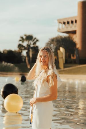 Golden sunset reflects on water while balloons float near an elegant modern building.