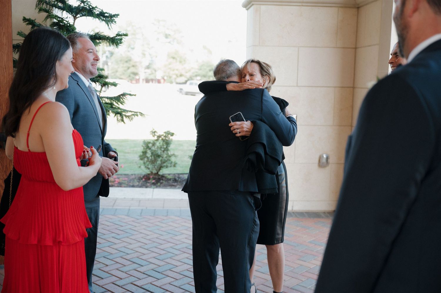 Wedding guests sharing emotional hugs under an archway during the celebration.
