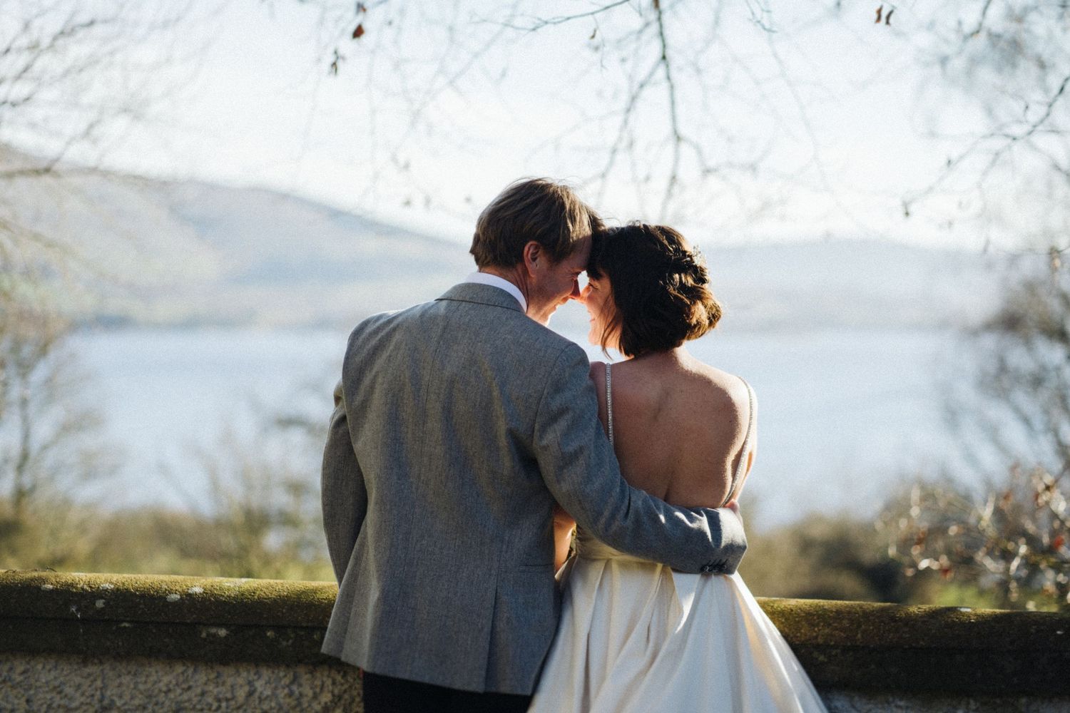 Intimate moment between newlyweds overlooking a serene lake landscape.