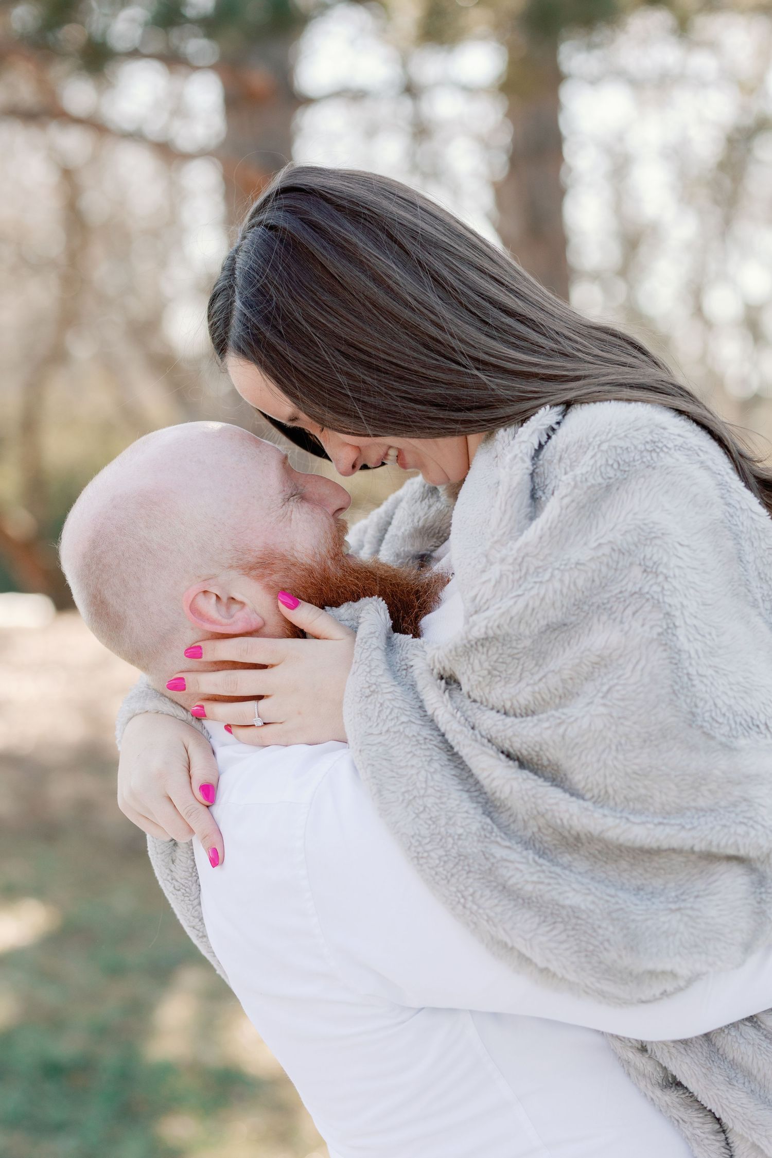 A man lifts his girlfriend who is wrapped in a blanket. They smile at each other, leaning into each other.