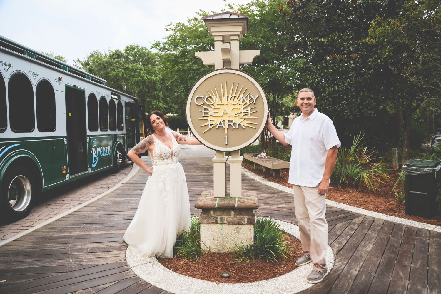 A couple poses with a decorative sun medallion at a resort boardwalk with a trolley in the background.