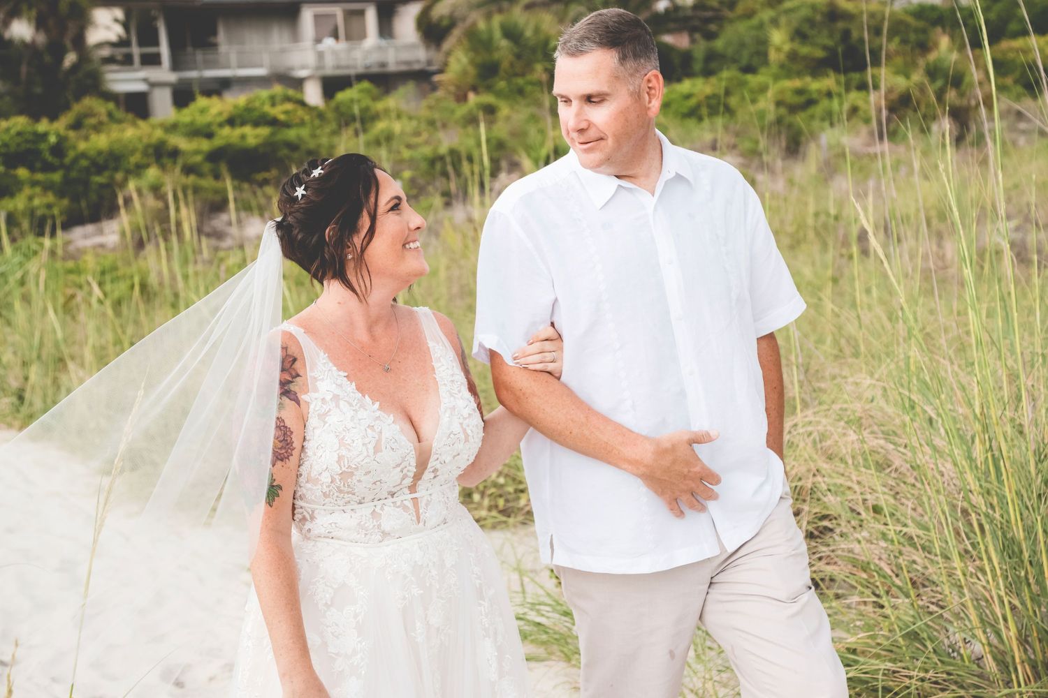 Newlyweds share a joyful moment together on beach path surrounded by sea grass.