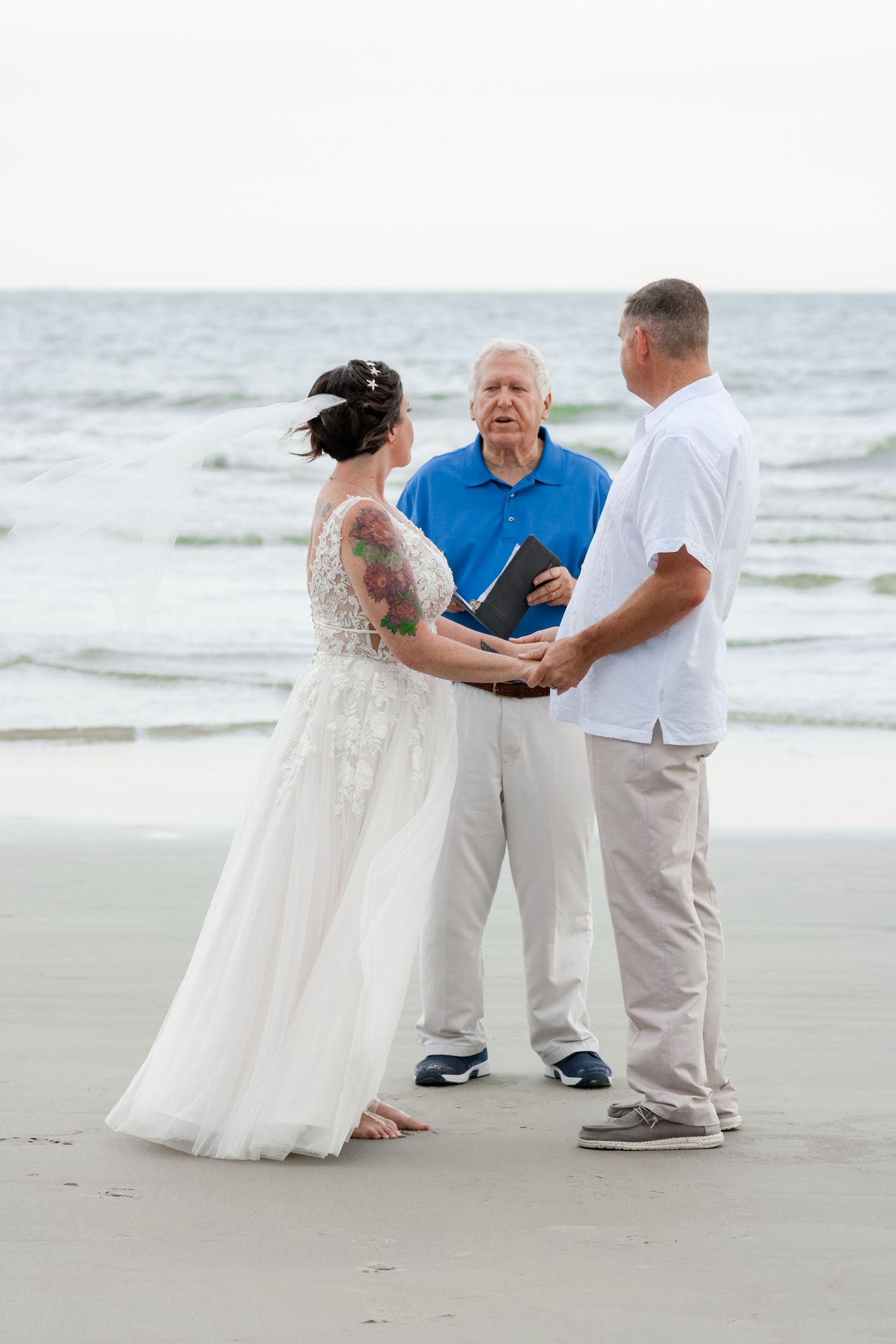 A beach wedding ceremony takes place on the sand with waves in the background at sunset.