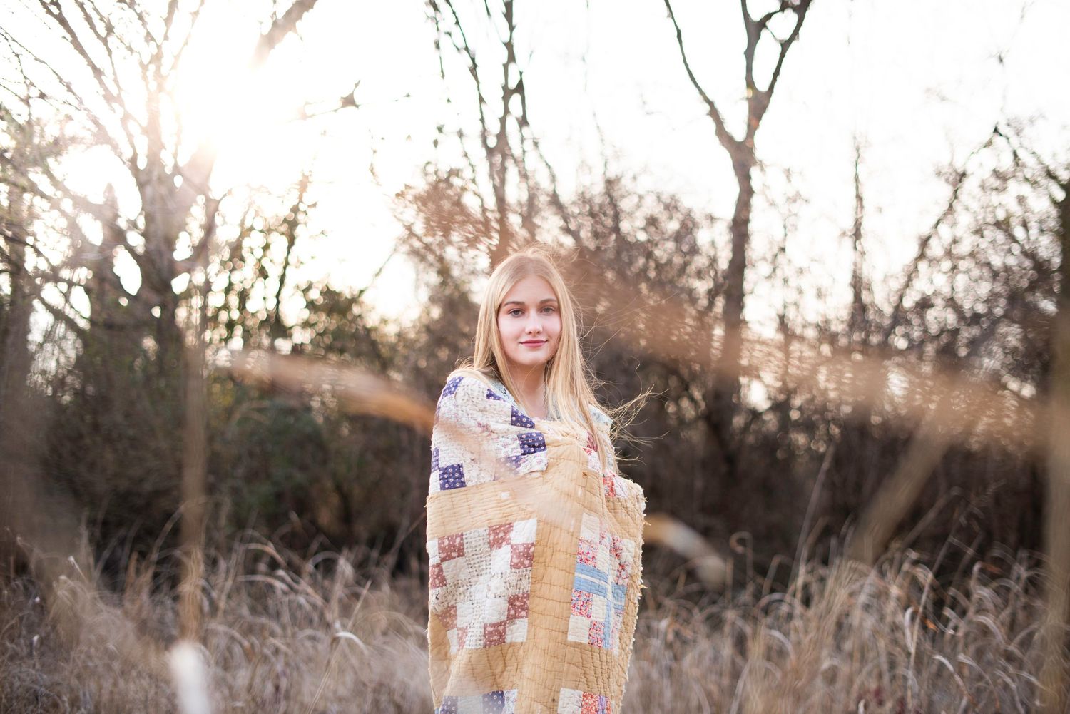 Person in floral dress posing in autumn field with sunlight streaming through trees.
