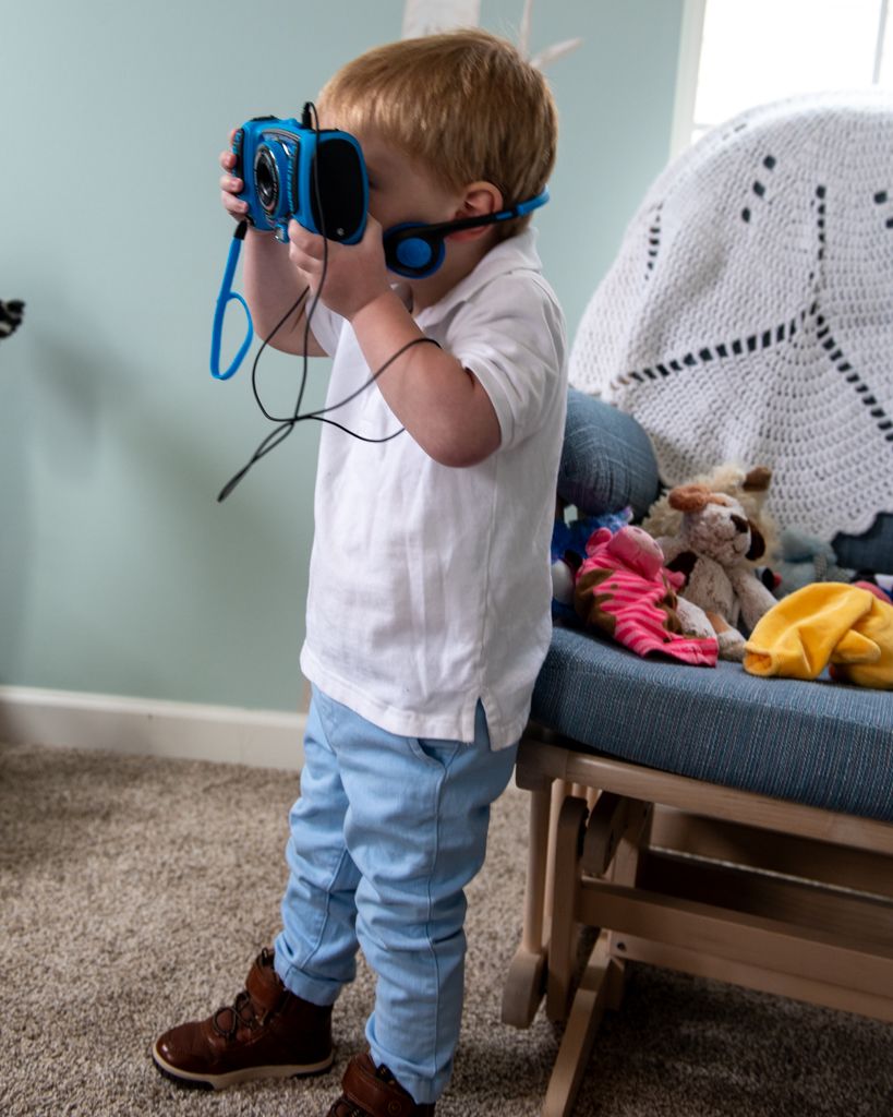 Small child holding a blue toy camera while standing in a room with a couch.