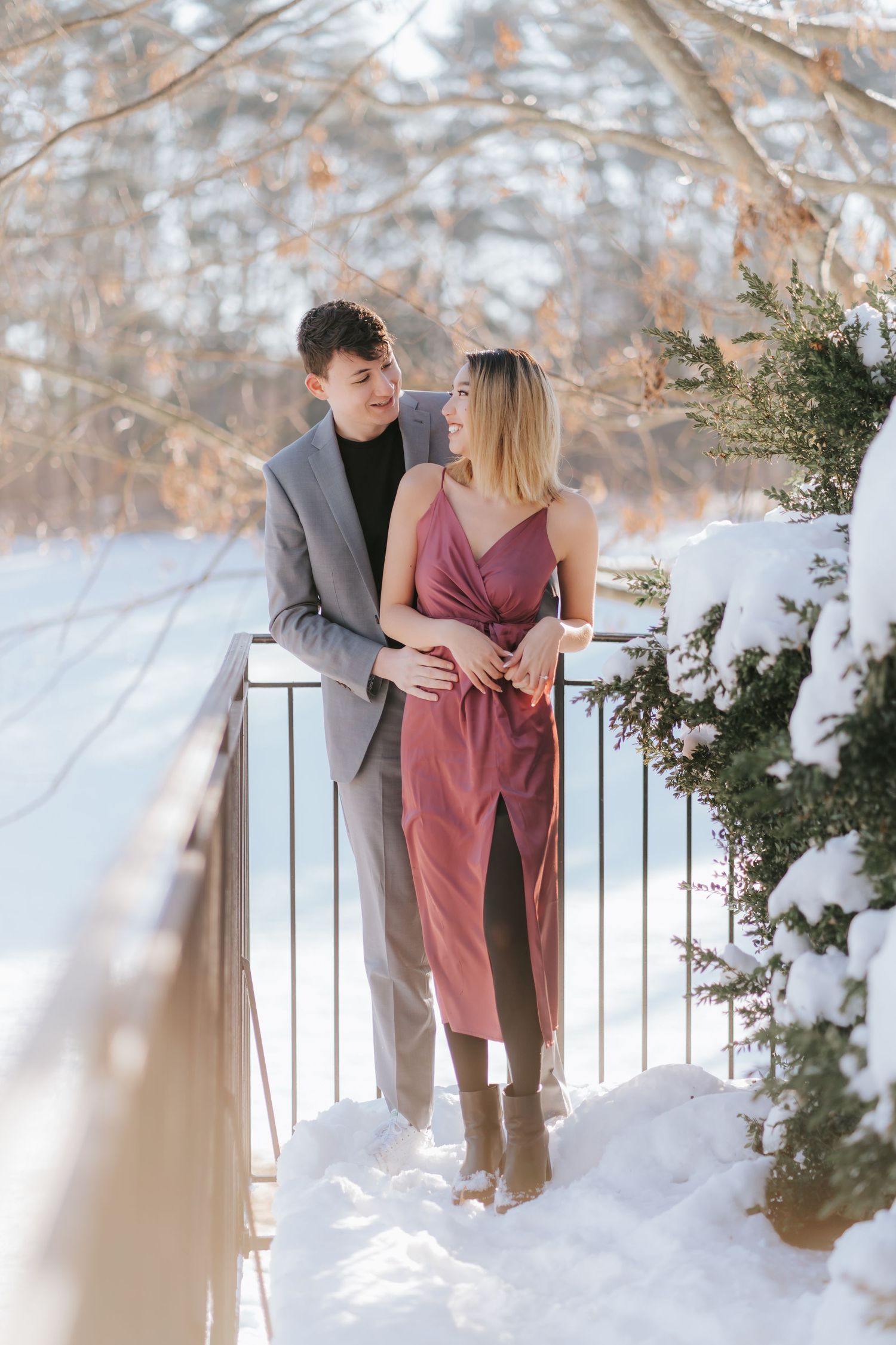 A couple embracing on a snowy balcony with winter trees in the background.