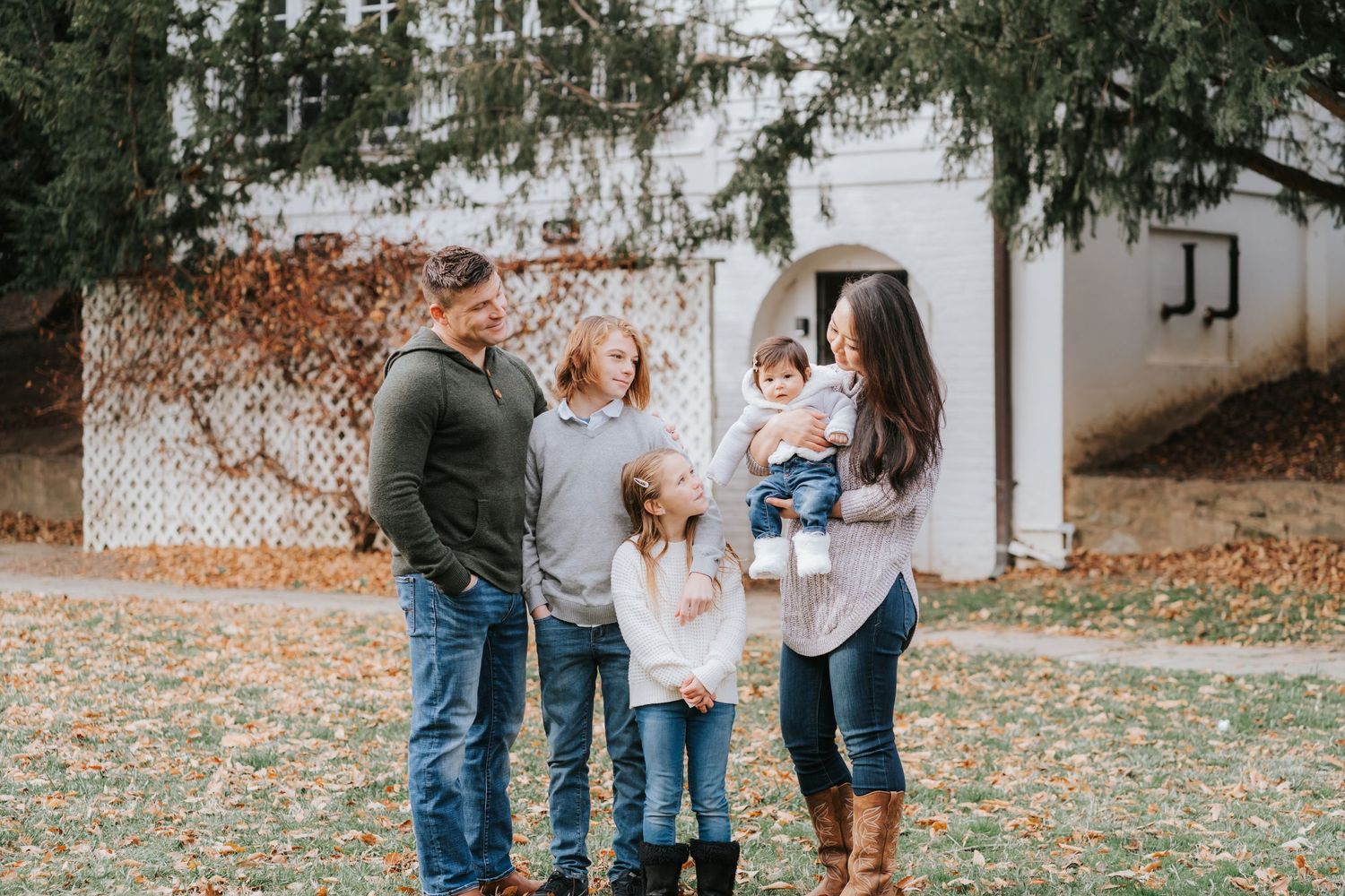 Family standing together on autumn leaves with white building in background.