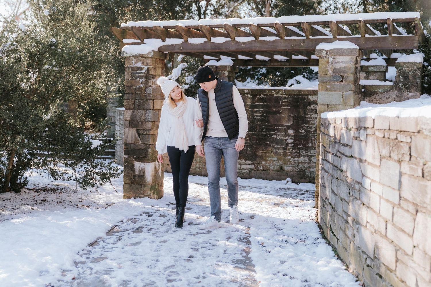 A couple walking together through a snow-covered stone archway in winter.