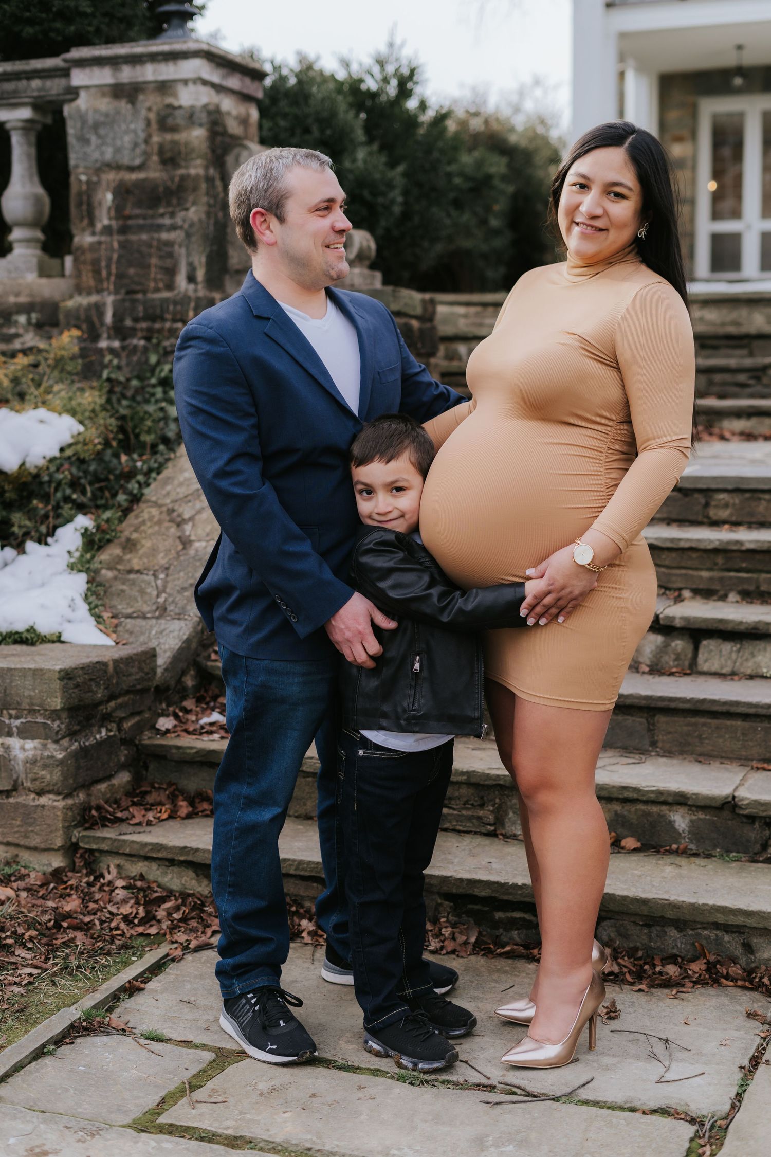 Family maternity photo on stone steps with couple and young child in coordinated outfits.