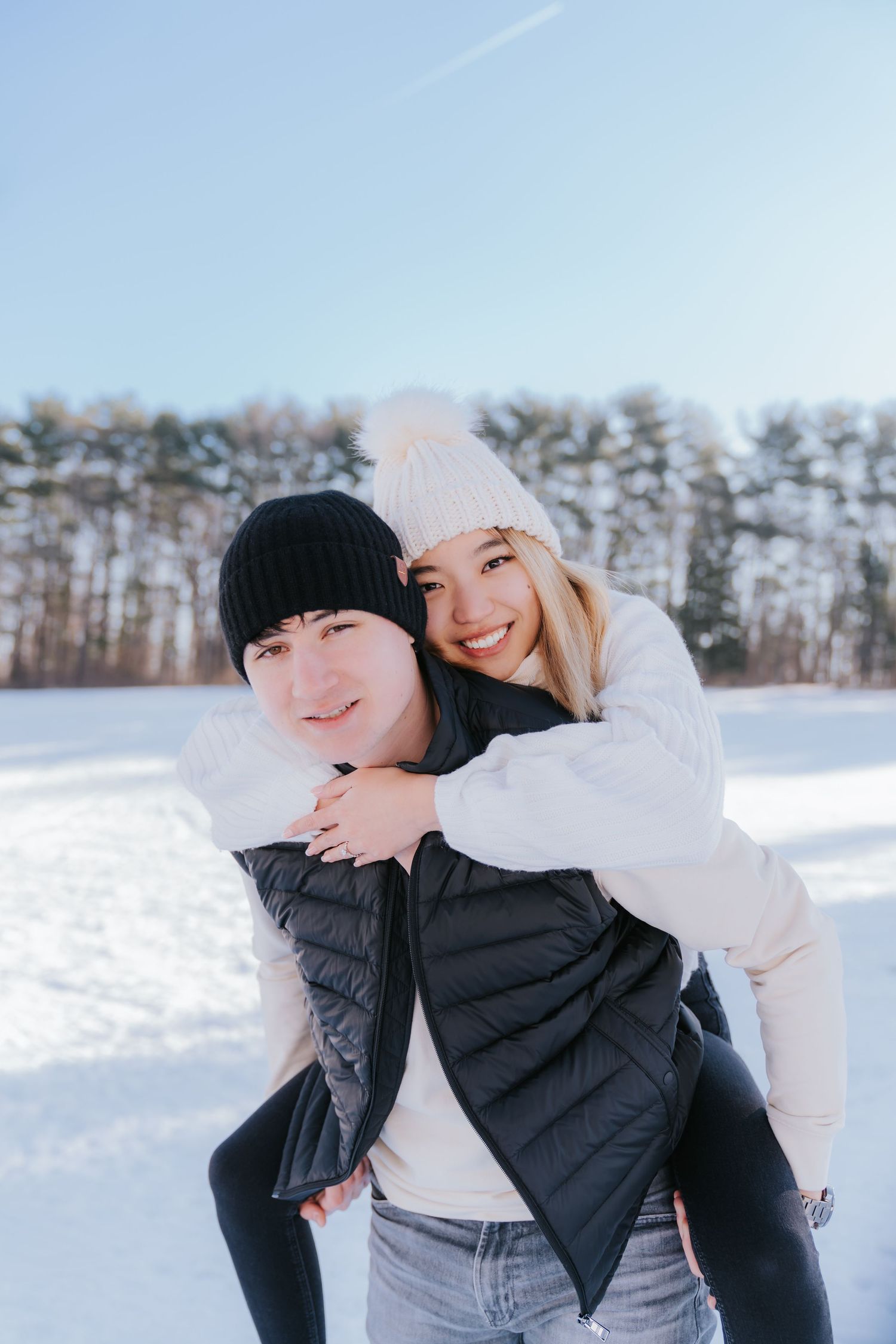 A playful piggyback ride in a snowy winter field with pine trees in the background.