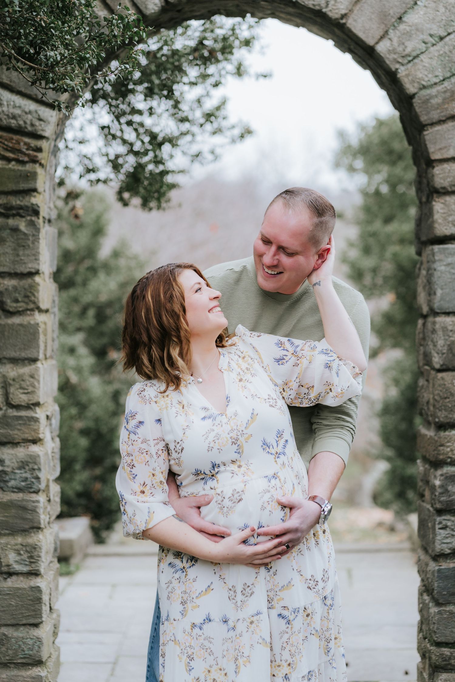 A romantic maternity photo of a couple under a stone archway.
