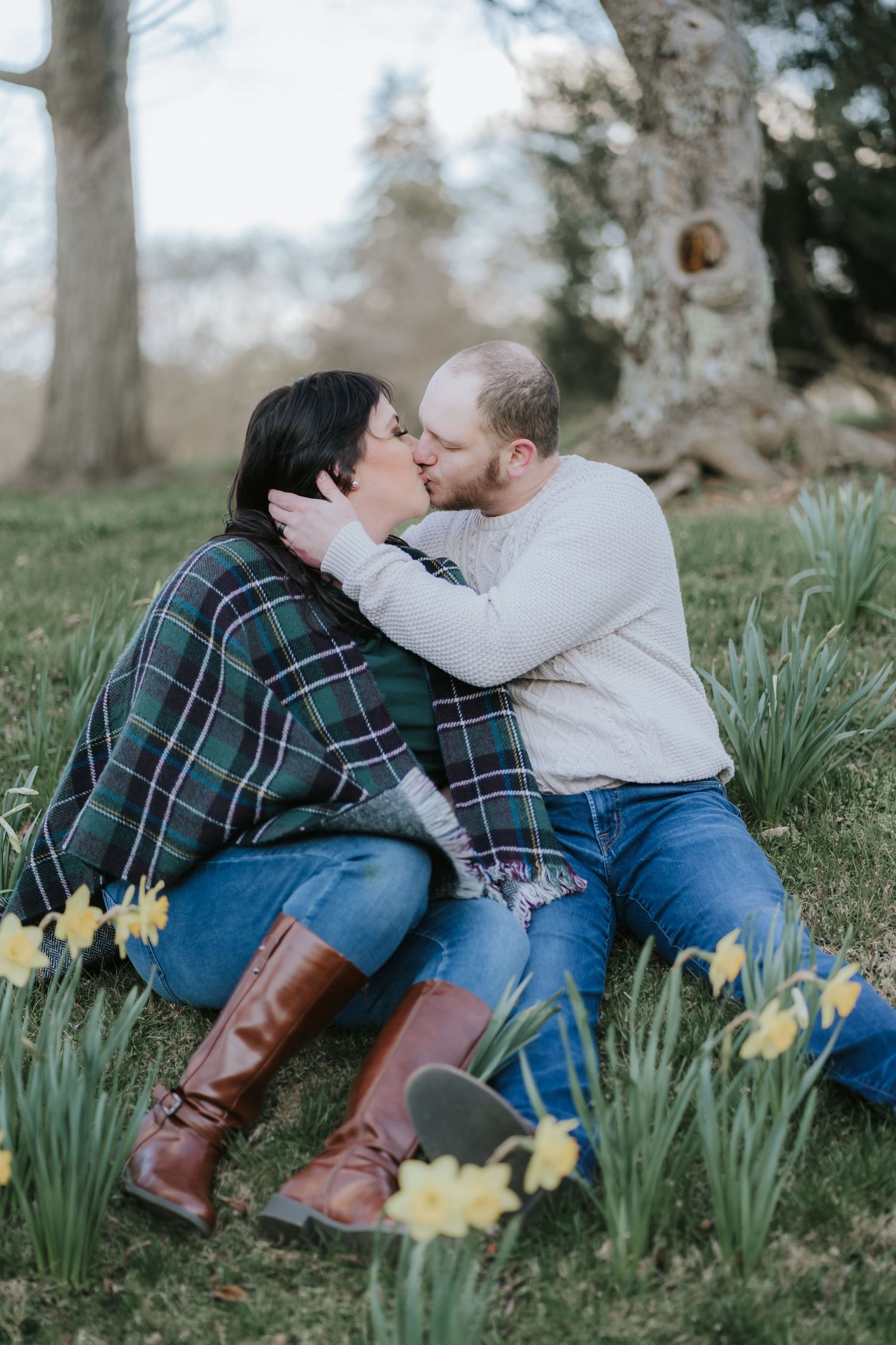 A couple shares a kiss while sitting among spring daffodils in a garden setting.